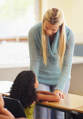 Buy stock photo Teacher, student and talking at desk for education, learning and knowledge in a classroom. Professional woman helping girl learn while teaching children at elementary school for development or lesson