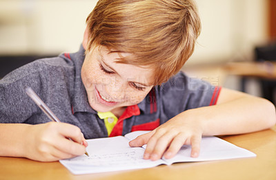 Buy stock photo School, education and a student boy writing in a book while sitting at his desk in a class room for learning. Kids, study and notebook with a young male pupil in a classroom for child development