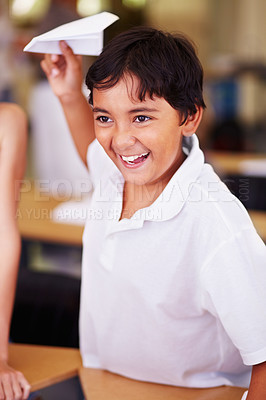 Buy stock photo School, classroom and a boy playing with a paper airplane while learning for education or child development. Study, children and growth with a male student having fun in an elementary class for kids