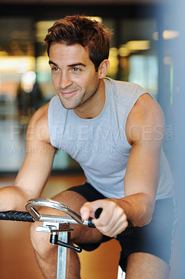 Buy stock photo A smiling handsome young man wearing sport clothing and using a exercise bike at the gym