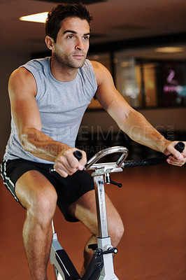 Buy stock photo A handsome young man wearing sport clothing and using a exercise bike at the gym