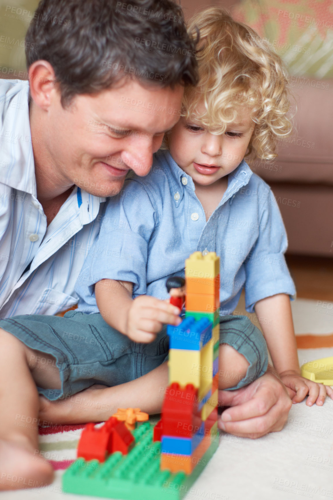 Buy stock photo A father watching his toddler son playing with building blocks