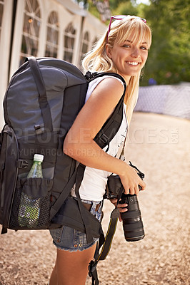 Buy stock photo A beautiful young photographer walking with gear on her back and camera in her hands
