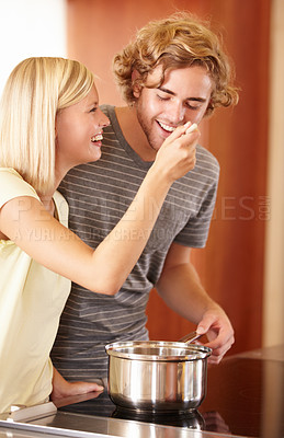 Buy stock photo A young man tasting his girlfriend's food in the kitchen