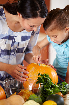 Buy stock photo A happy young mother helping her daughter to carve a pumpkin in the kitchen