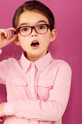 Buy stock photo A little girl with expression of surprise holding the edge of her spectacles against a pink background