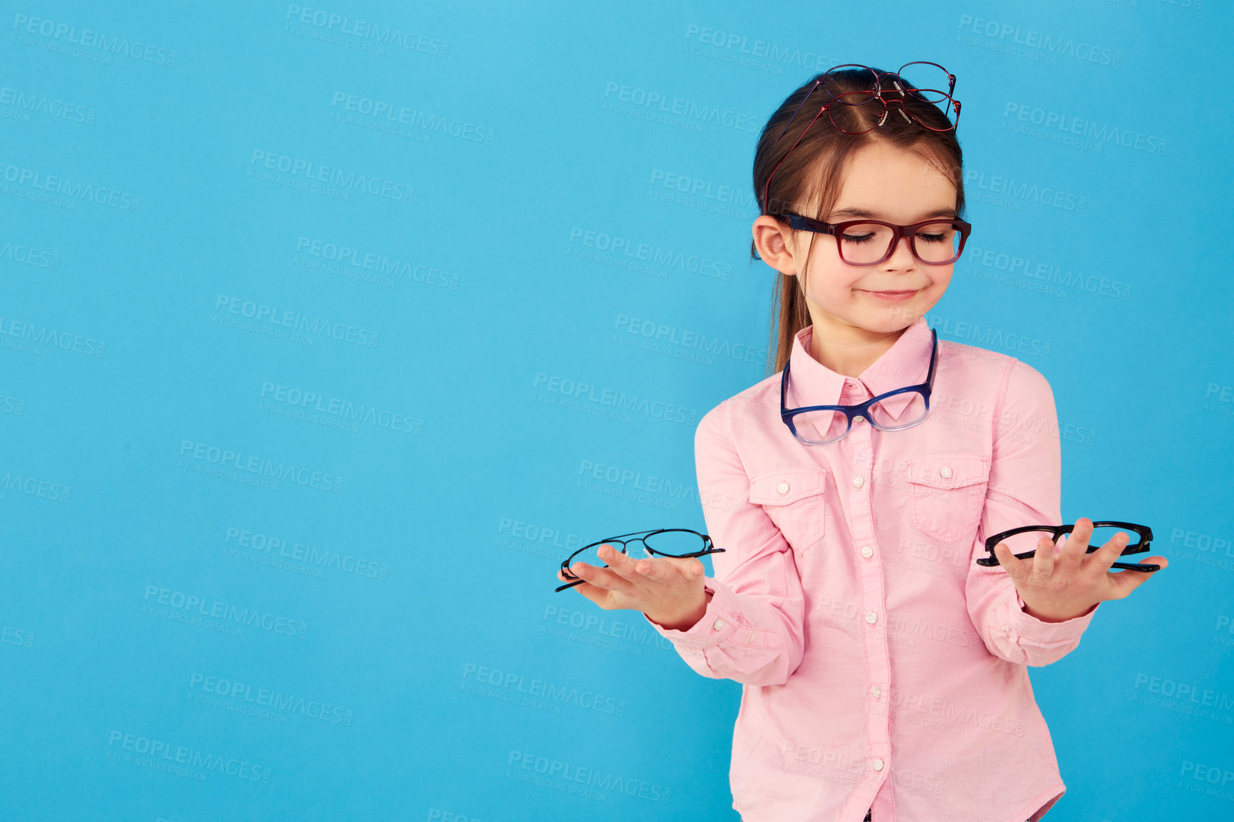 Buy stock photo Happy, decision and a girl with optometry glasses isolated on a blue background in studio. Smile, young and a little child with eyewear choice for vision, eyesight and choosing spectacles with mockup
