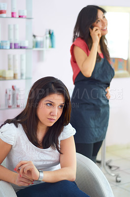 Buy stock photo A young woman looking annoyed as she waits for her stylist to finish a personal call