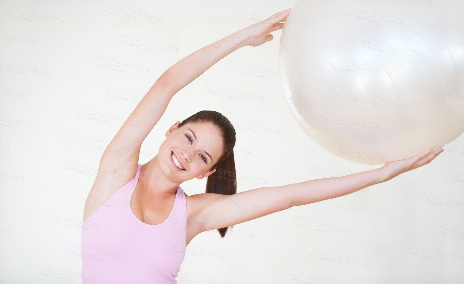 Buy stock photo Shot of an attractive young woman with her arms stretched above her head holding an exercise ball