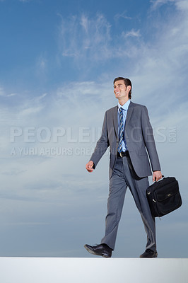 Buy stock photo A young businessman carrying his briefcase against a blue sky