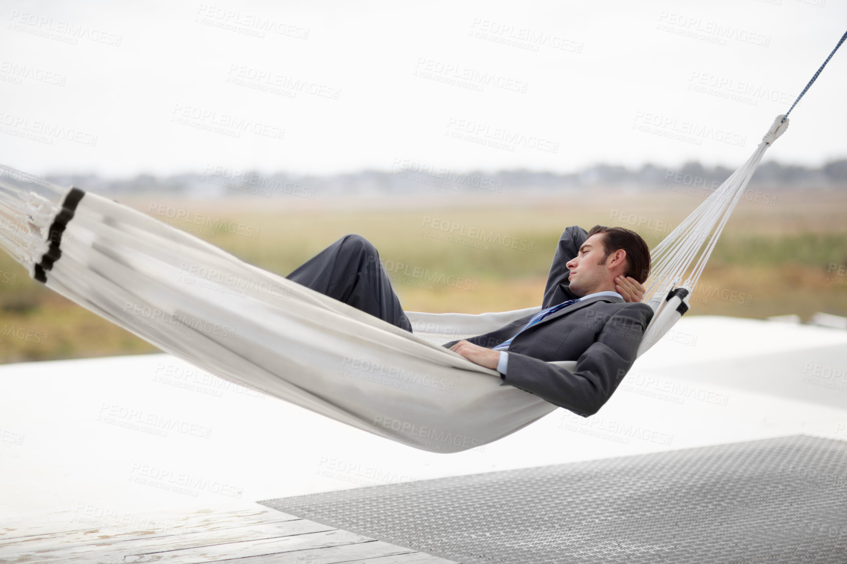 Buy stock photo A young executive in a suit taking in the landscape from a hammock