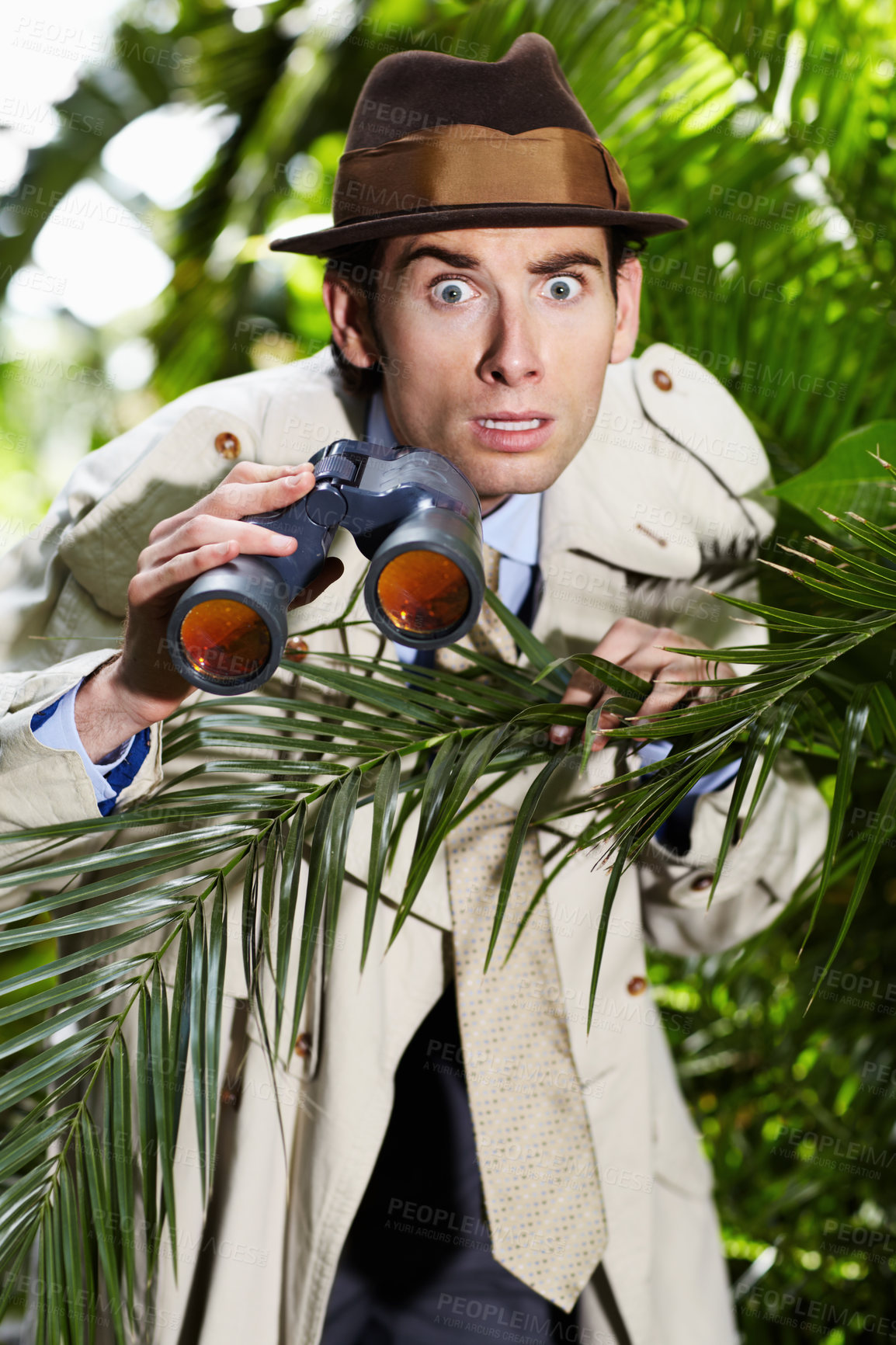 Buy stock photo Shocked private investigator using binoculars to spy on someone from the bushes