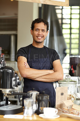 Buy stock photo Shot of a handsome barista standing behind his coffee bar with his arms crossed