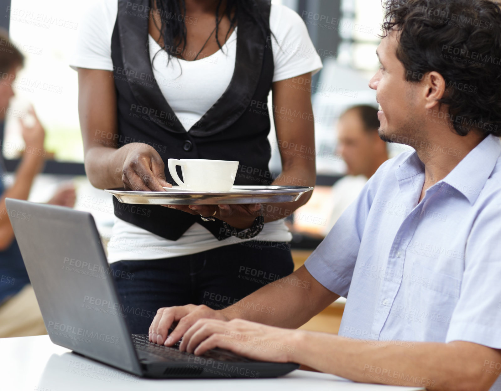 Buy stock photo Shot of a waitress delivering a coffee to a man working on a laptop