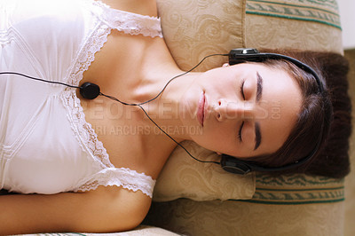 Buy stock photo An attractive young woman listening to music while dozing on the sofa