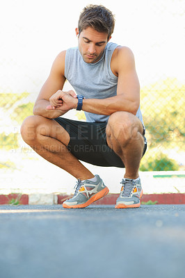 Buy stock photo Young athlete squatting down and taking a look at his watch