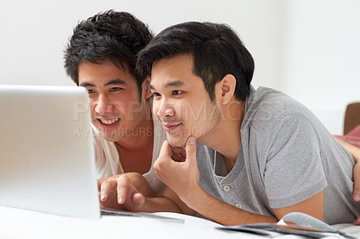 Buy stock photo Two young Asian guys searching the internet together on a laptop