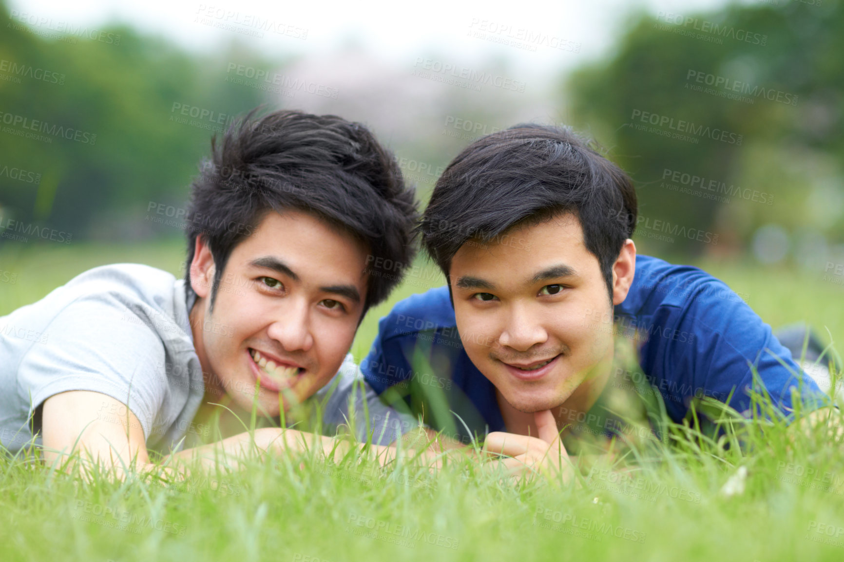 Buy stock photo Cute young gay Asian couple smiling together while lying on the grass