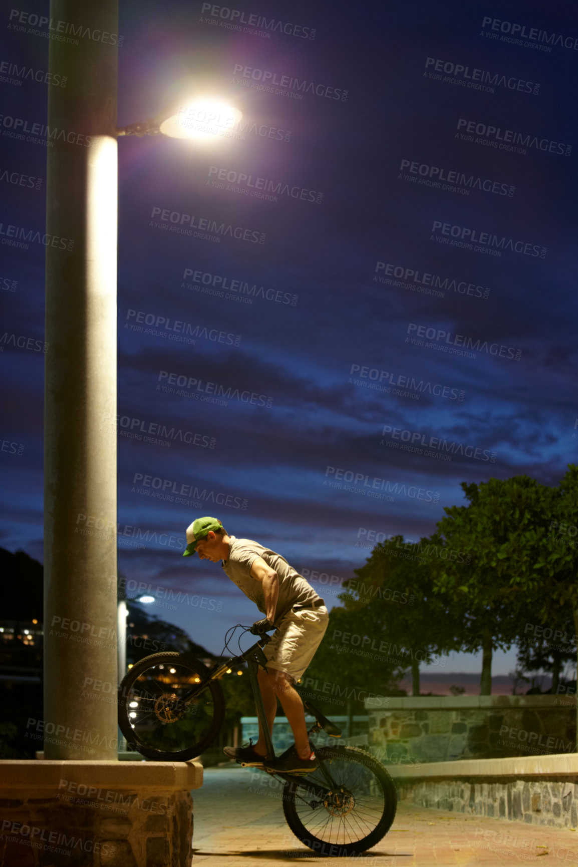 Buy stock photo Shot of a man doing tricks on his bike at night under a street light
