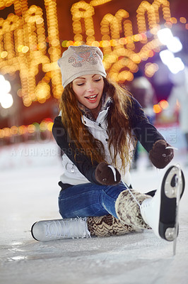 Buy stock photo Shot of a young woman sitting on the ice of a skating rink tying the laces of her ice skates