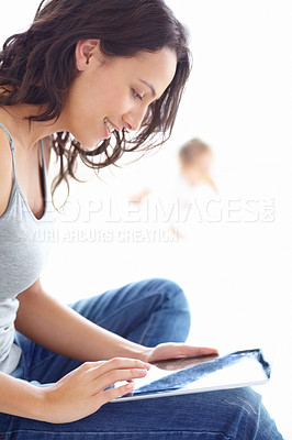 Buy stock photo An attractive young mother working on her tablet with her baby in the background