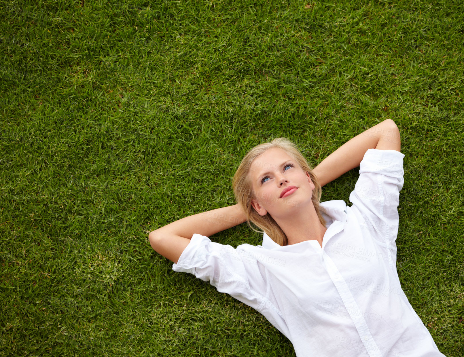 Buy stock photo High angle shot of an attractive young woman relaxing on a grassy field and looking up at the sky