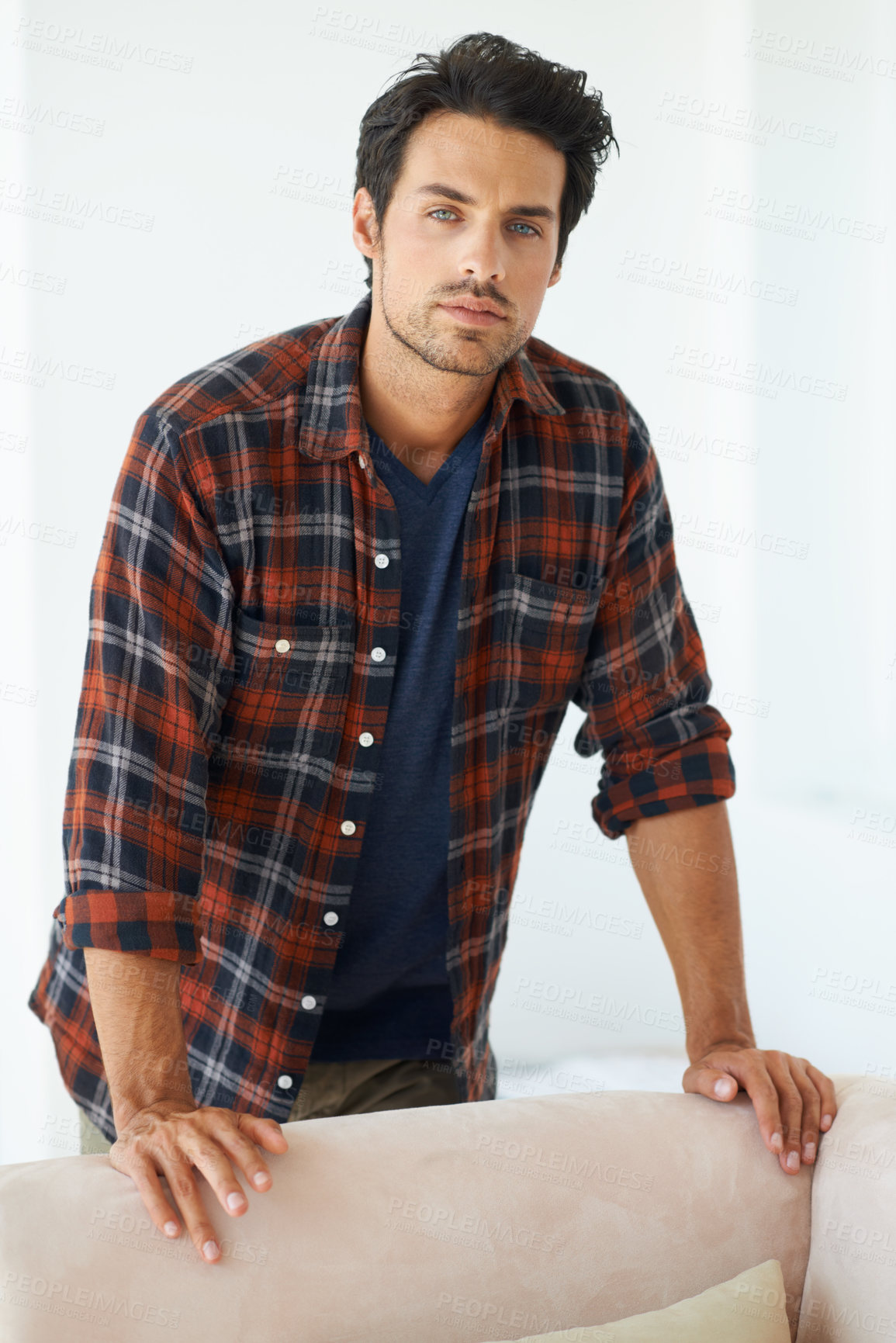 Buy stock photo Portrait of a gorgeous young man standing behind a sofa and looking at the camera