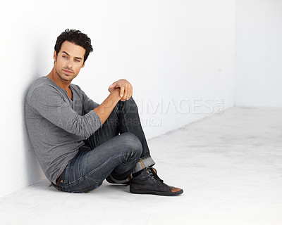 Buy stock photo Handsome, fashion and young man by a white wall with casual, cool and trendy outfit. Attractive, confidence and serious male model from Canada sitting on floor with edgy style for aesthetic.