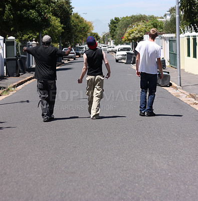 Buy stock photo Shot of three young men walking down a suburban street