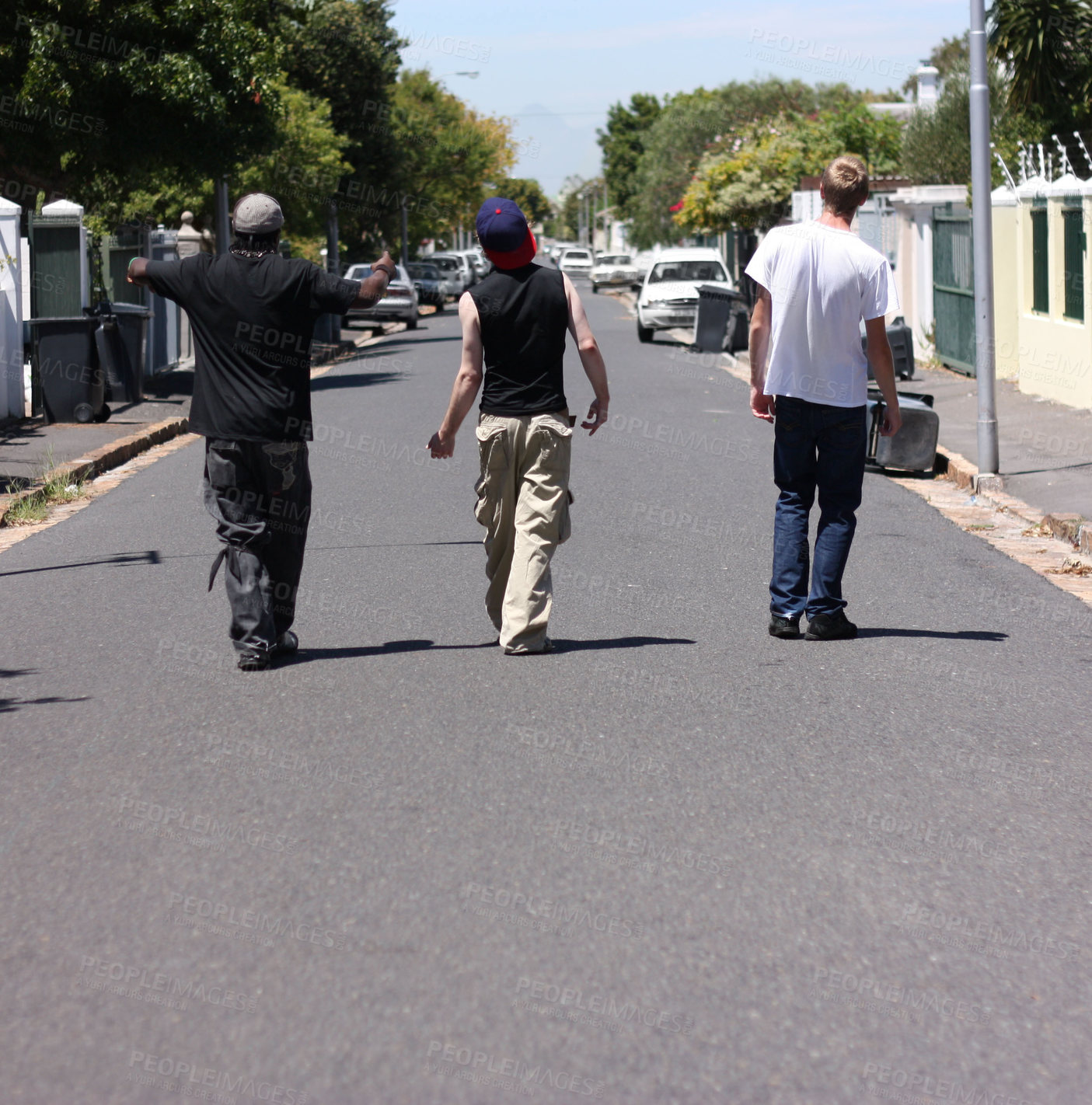 Buy stock photo Shot of three young men walking down a suburban street
