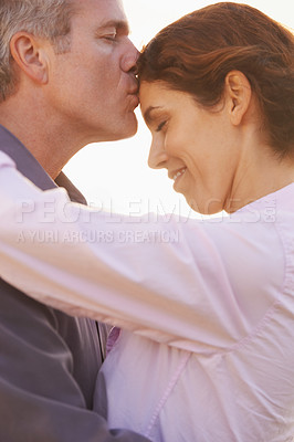 Buy stock photo Couple, forehead kiss and hug with love, respect or happiness on holiday in retirement. Mature, man and woman embrace together outdoor at sunset on vacation or show affection or gratitude in marriage