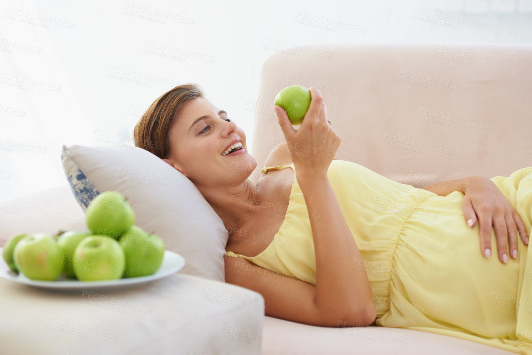 Buy stock photo Pregnant woman, apple and smile on sofa for health, nutrition and wellness in living room of apartment. Person, fruit and happy on couch of lounge for relax, pregnancy and healthy diet with vitamins