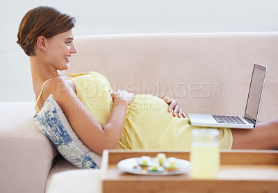 Buy stock photo A smiling pregnant woman lying on the couch using a laptop with a healthy meal beside her