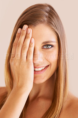 Buy stock photo Studio portrait of a young woman with one hand over one eye smiling at the camera