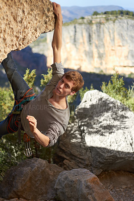 Buy stock photo Portrait of a rock climber dangling from one hand off the edge of a cliff with view of mountains in the background