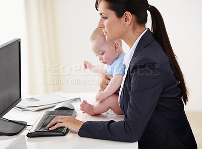 Buy stock photo Young working mother holding a baby while working on her computer
