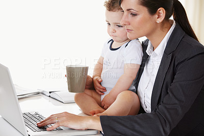 Buy stock photo Young working mother holding a baby while working and drinking coffee