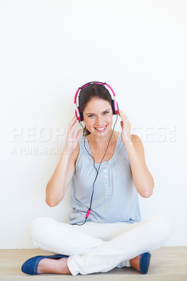 Buy stock photo Portrait, woman and music on a floor with headphones in studio, happy and streaming on a wall background. Face, smile and girl relax with podcast, radio or audio track while sitting against mockup