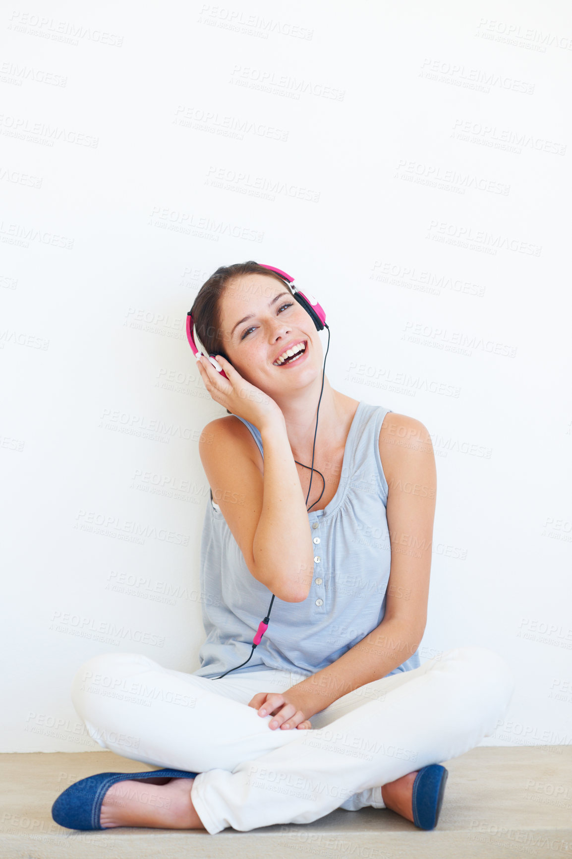 Buy stock photo Headphones, music and portrait of woman on a floor in studio, happy and streaming on a wall background. Face, smile and girl relax with podcast, radio or audio track while sitting against mockup