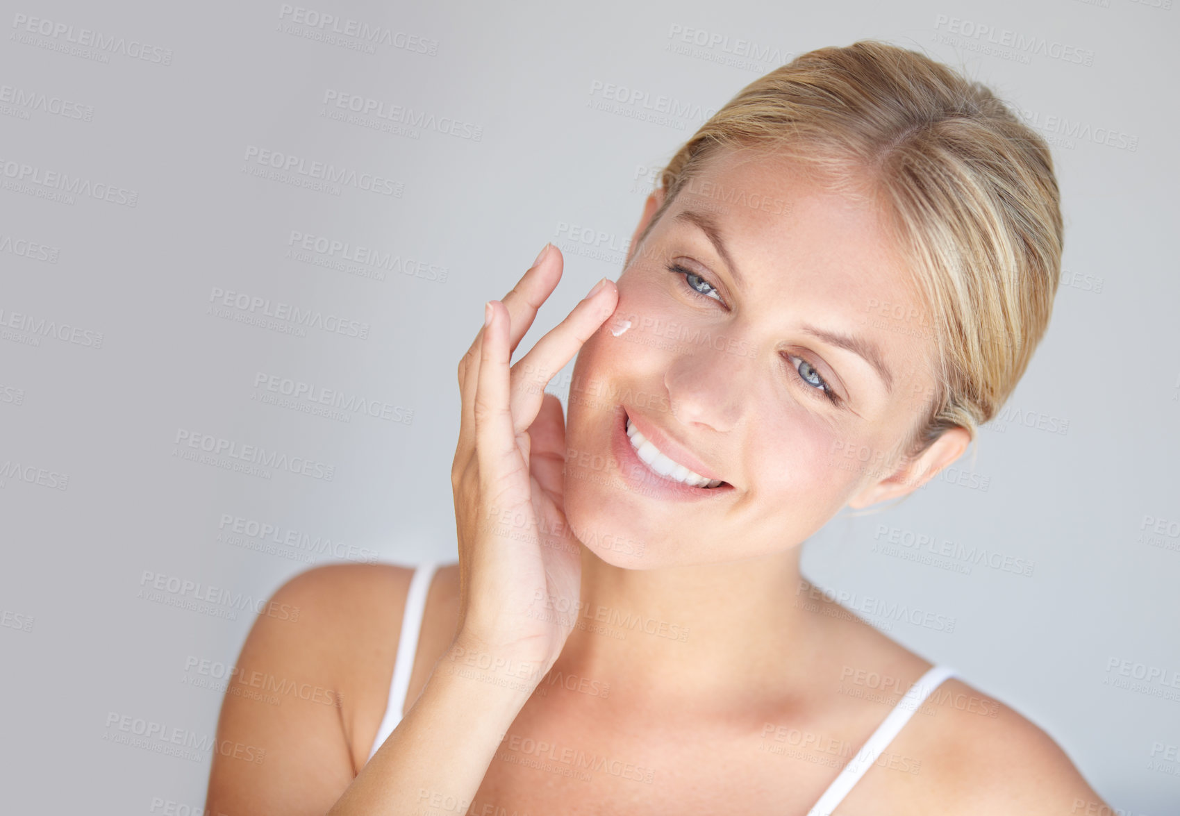 Buy stock photo Smile, skincare and woman with cream, cosmetics and dermatology against a grey studio background. Female person, model or girl with lotion, touching face and pamper treatment with grooming and beauty