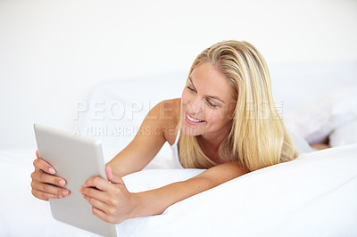 Buy stock photo A beautiful young blonde woman working on her digital touchpad while lying in bed