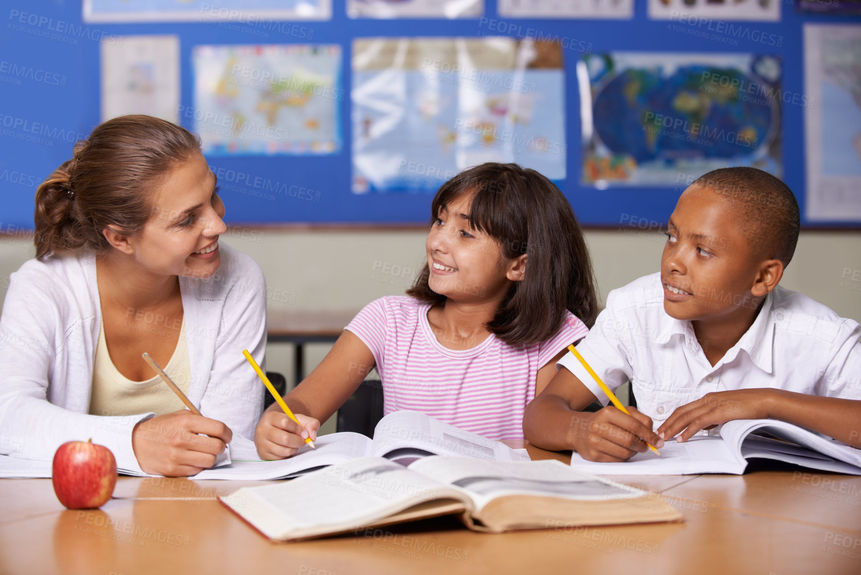 Buy stock photo A young teacher having a discussion with her two ethnic pupils while they page through a textbook