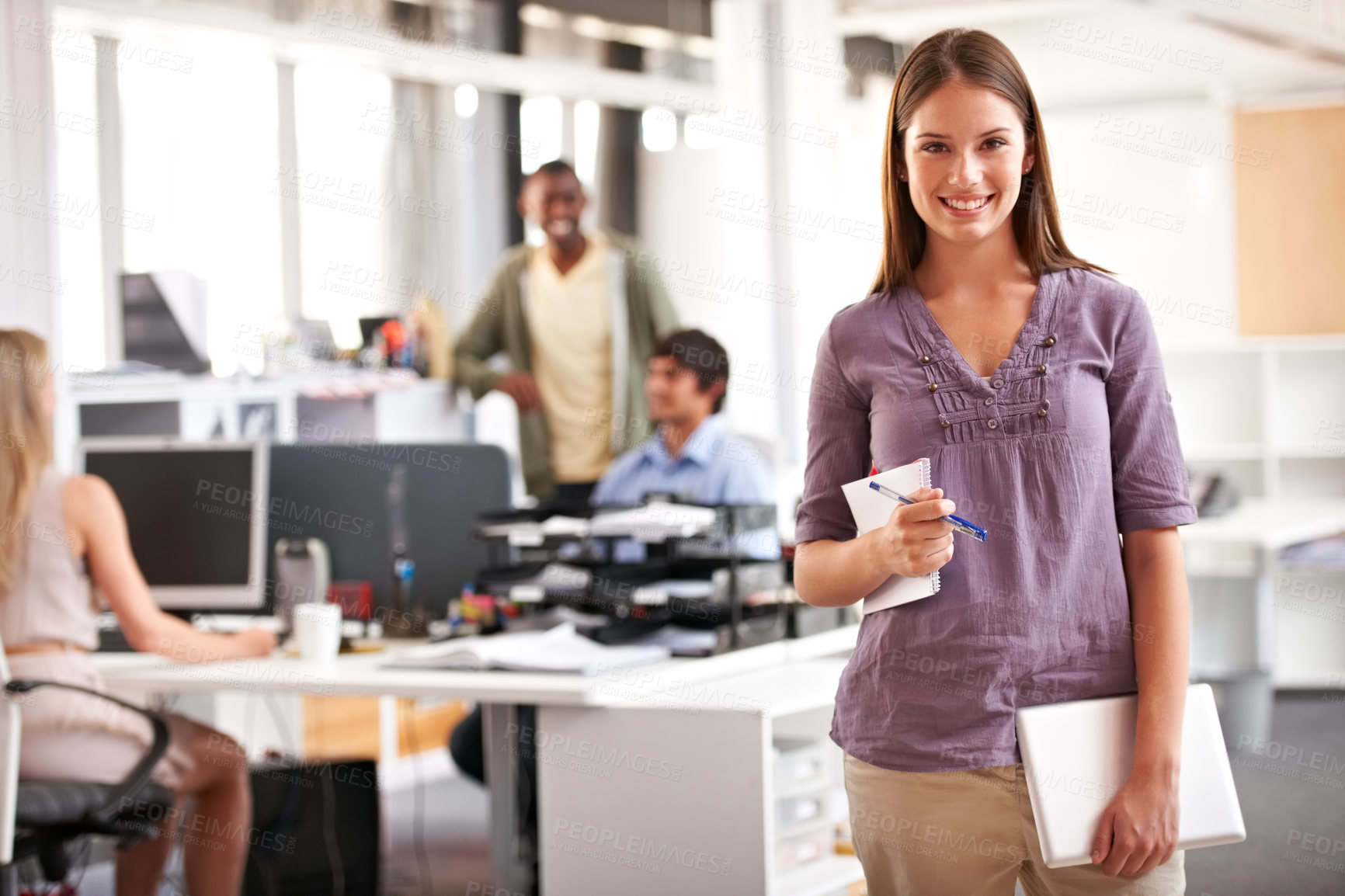Buy stock photo Shot of a young designer holding her notepad and digital tablet with her colleagues in the background