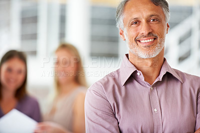 Buy stock photo Shot of a leader smiling at the camera with colleagues blurred in the background