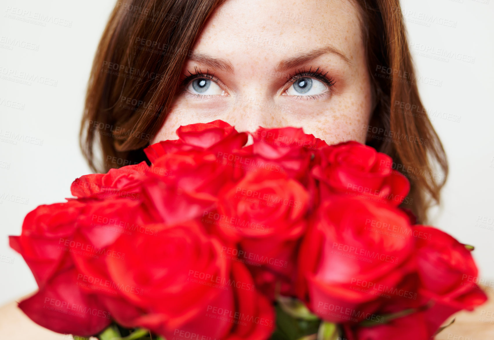 Buy stock photo An attractive young woman peering over a bouquet of roses