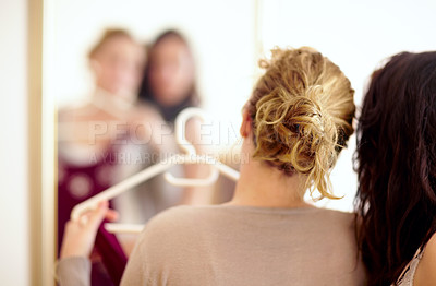 Buy stock photo Rearview shot of two sister looking at their reflection in a mirror while trying to pick some clothing