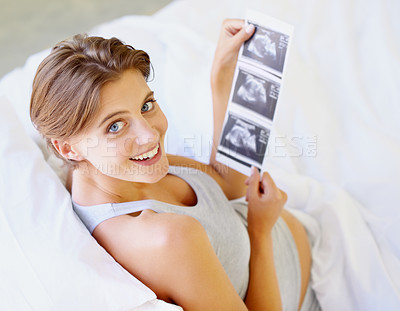 Buy stock photo A high-angle view of a pregnant woman looking up at the camera while holding a sonogram picture