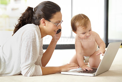Buy stock photo A young mother speaking on the phone while lying with her baby in front of an open laptop