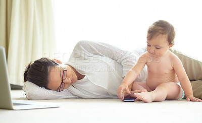 Buy stock photo An exhausted young mother lying asleep on the floor with her baby sitting next to her