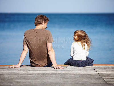 Buy stock photo Rear-view of a young father and his daughter sitting on a pier with the ocean in the background
